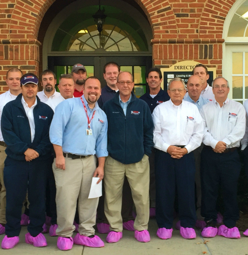 Group of Arrow Exterminators team members posed in front of a brick building wearing pink shoe protectors. 